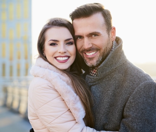 Man and woman in winter clothes hugging and smiling after cosmetic dentistry in New York