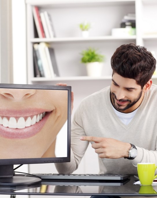 Man pointing to computer monitor showing close up of flawless smile
