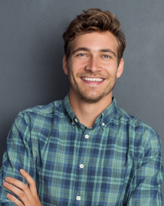 Young man in plaid shirt smiling with arms crossed