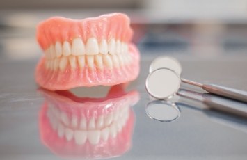 Set of full dentures next to dental mirror