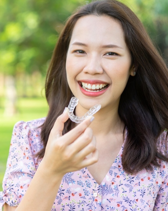 Woman smiling outdoors and holding an Invisalign tray