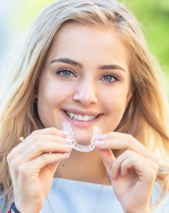 Smiling woman holding an Invisalign aligner near her mouth