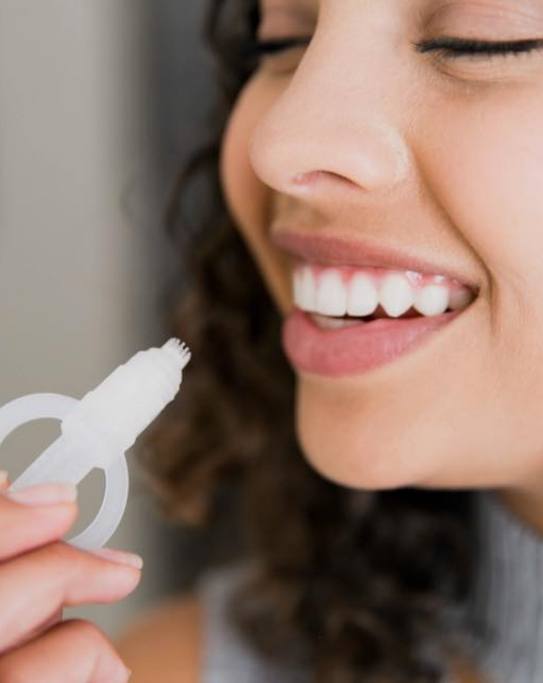 Woman holding teeth whitening applicator close to her teeth
