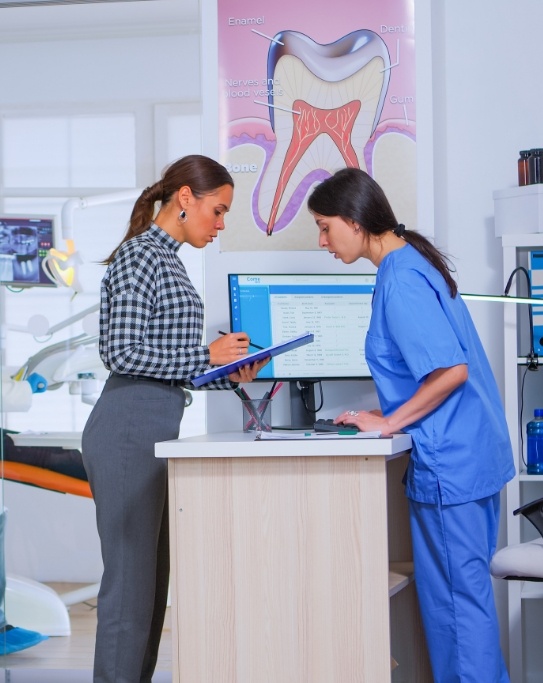 Woman with clipboard talking to dental team member at desk