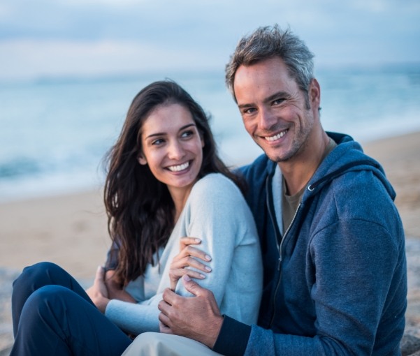 Smiling man and woman sitting together on beach after visiting New York dental office