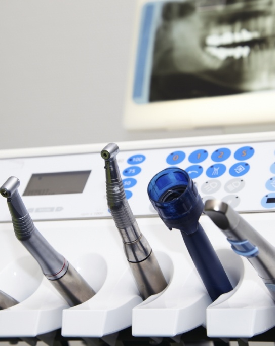 Row of dental instruments with x ray of teeth on screen in background