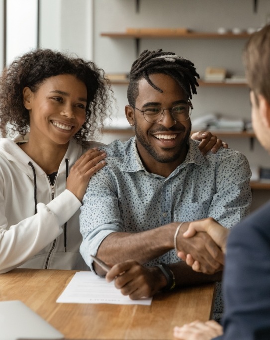 Smiling man shaking hands with person sitting across desk