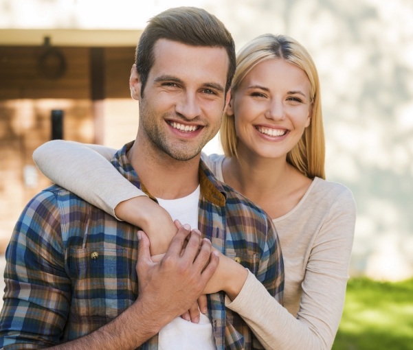 Young man and woman smiling and hugging outdoors after dental services in New York