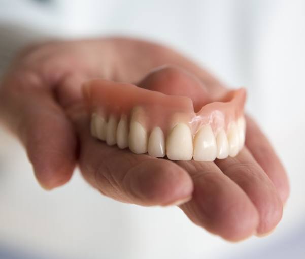 Hand holding a full denture in New York