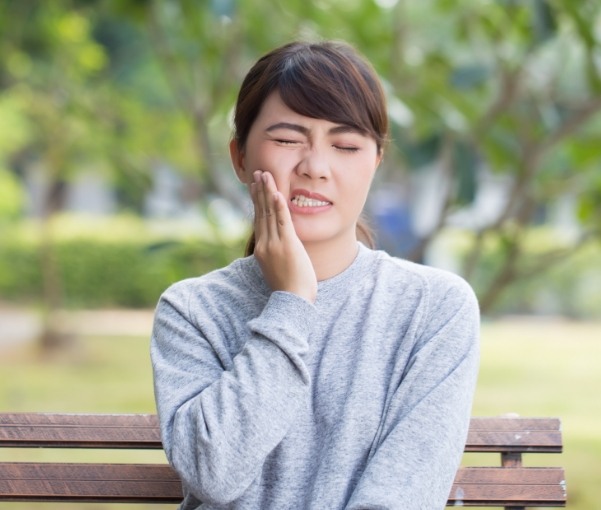 Wincing woman holding her cheek needing emergency dentist in New York