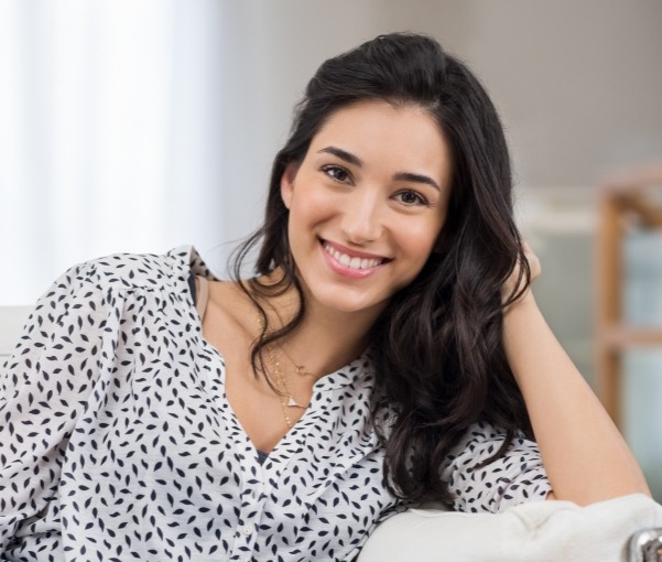 Woman sitting on couch and smiling after full mouth reconstruction in New York