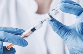 Dentist drawing syringe from vial of clear liquid