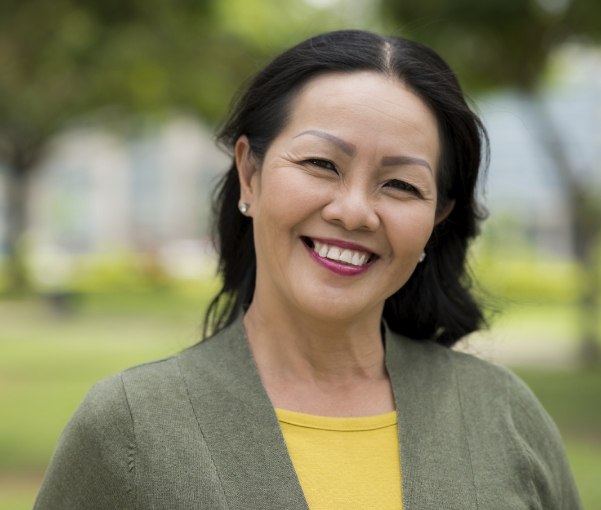 Woman in green jacket smiling outdoors after restorative dentistry in New York